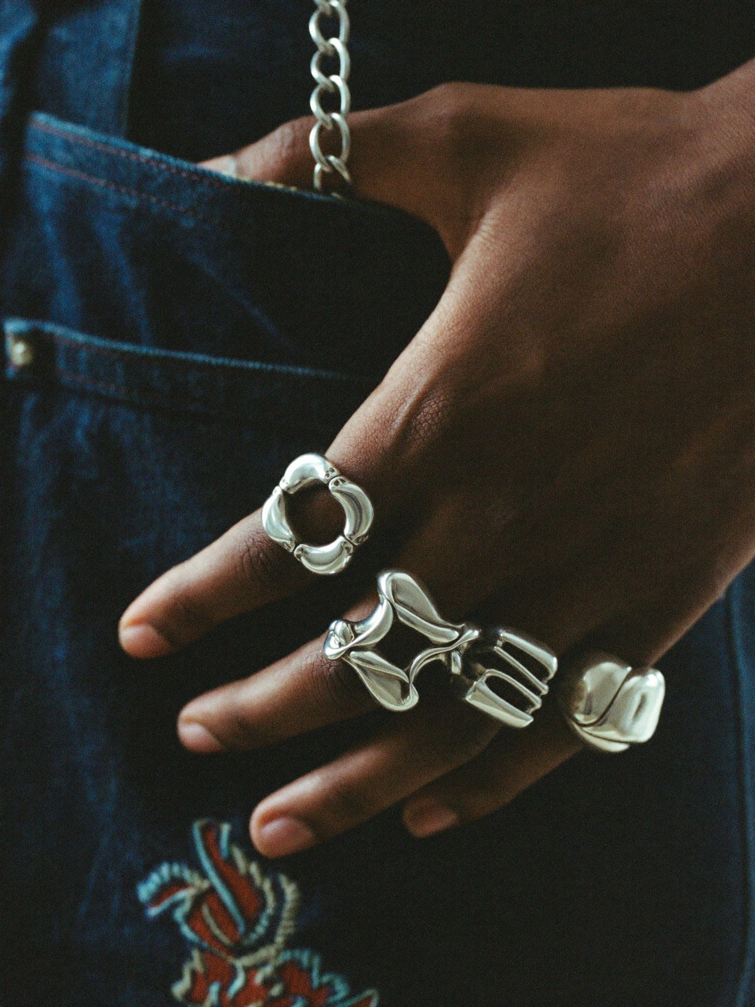 A hand wearing three heavy molten-looking silver rings, resting against indigo denim