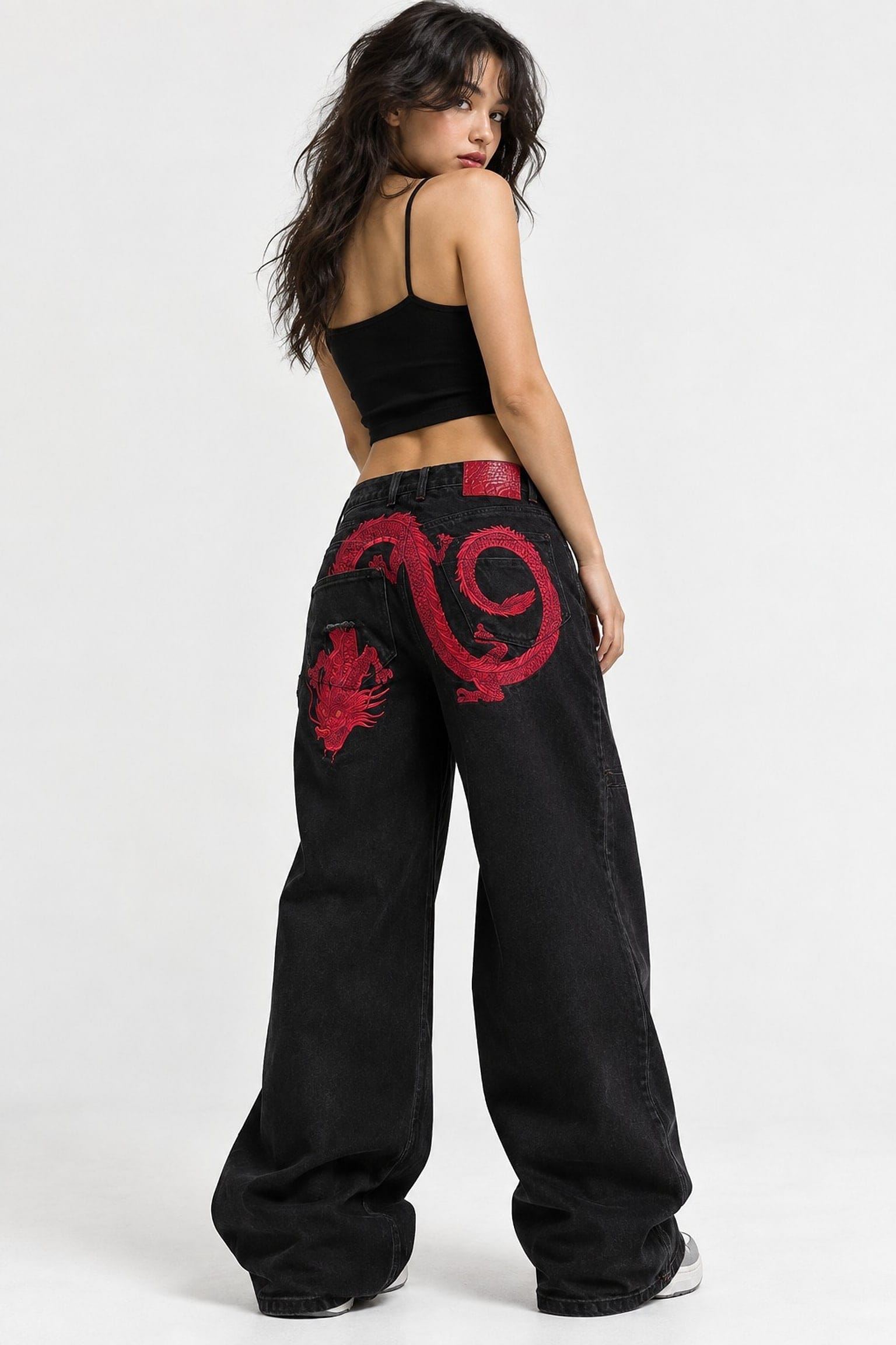 Model seen from behind in washed-black wide jeans, a red embroidered dragon coiling across both back pockets
