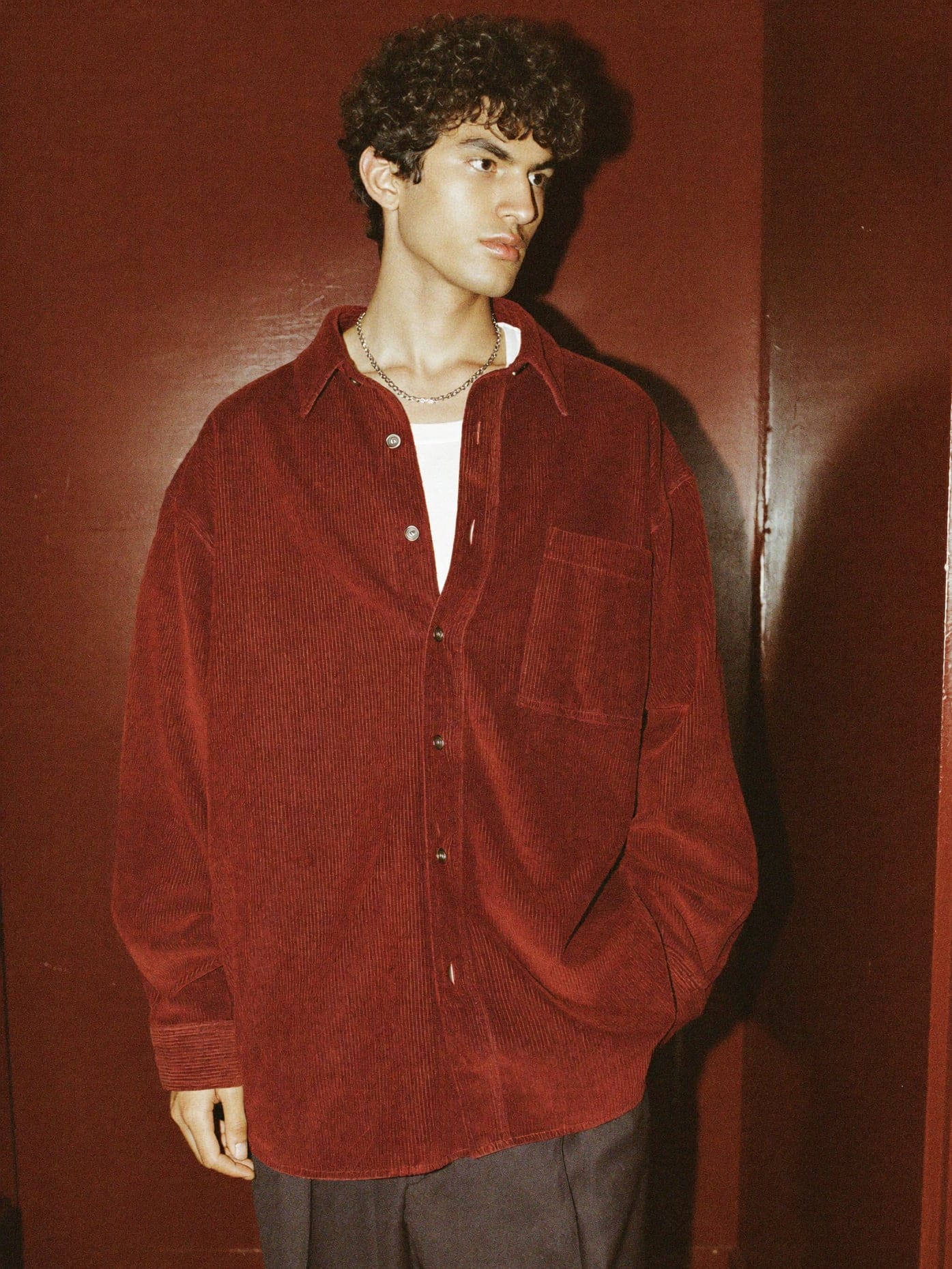 Model in an oxblood corduroy overshirt standing in a red-painted hallway